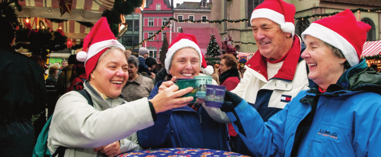 A group of people in Austria are wearing santa claus hats and clinking mugs together in a toast.